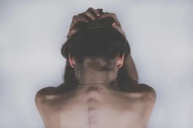 Personne de dos, mains dans les cheveux, illustrant les douleurs diffuses liées à la fibromyalgie