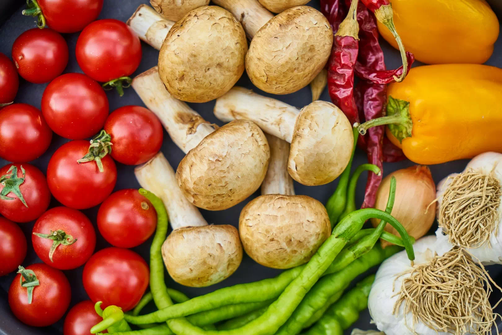 Assortiment de légumes frais illustrant une alimentation vegan, incluant champignons, tomates et poivrons.
