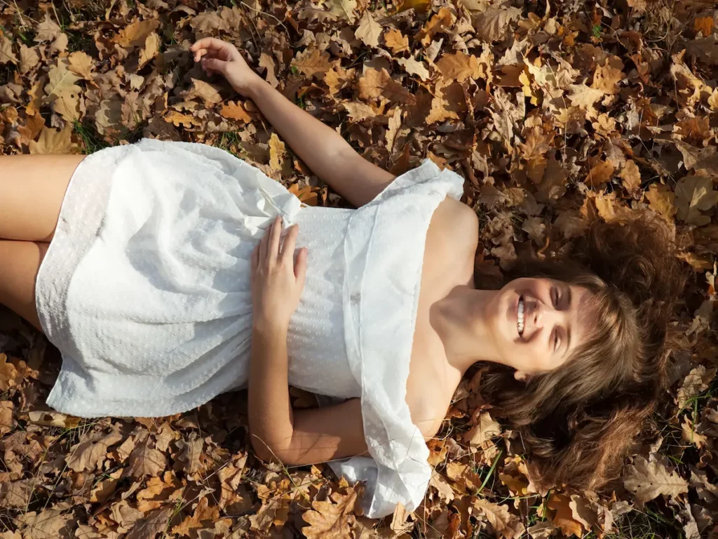 Femme allongée dans les feuilles d'automne, main sur l'abdomen, illustrant le lien intestin-cerveau en naturopathie