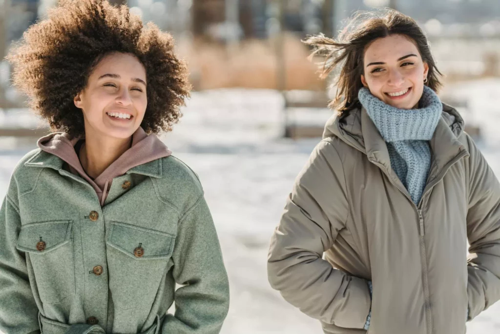 Deux femmes souriantes en extérieur sous la neige illustrant l'importance du lien social pour garder sa motivation en hiver.