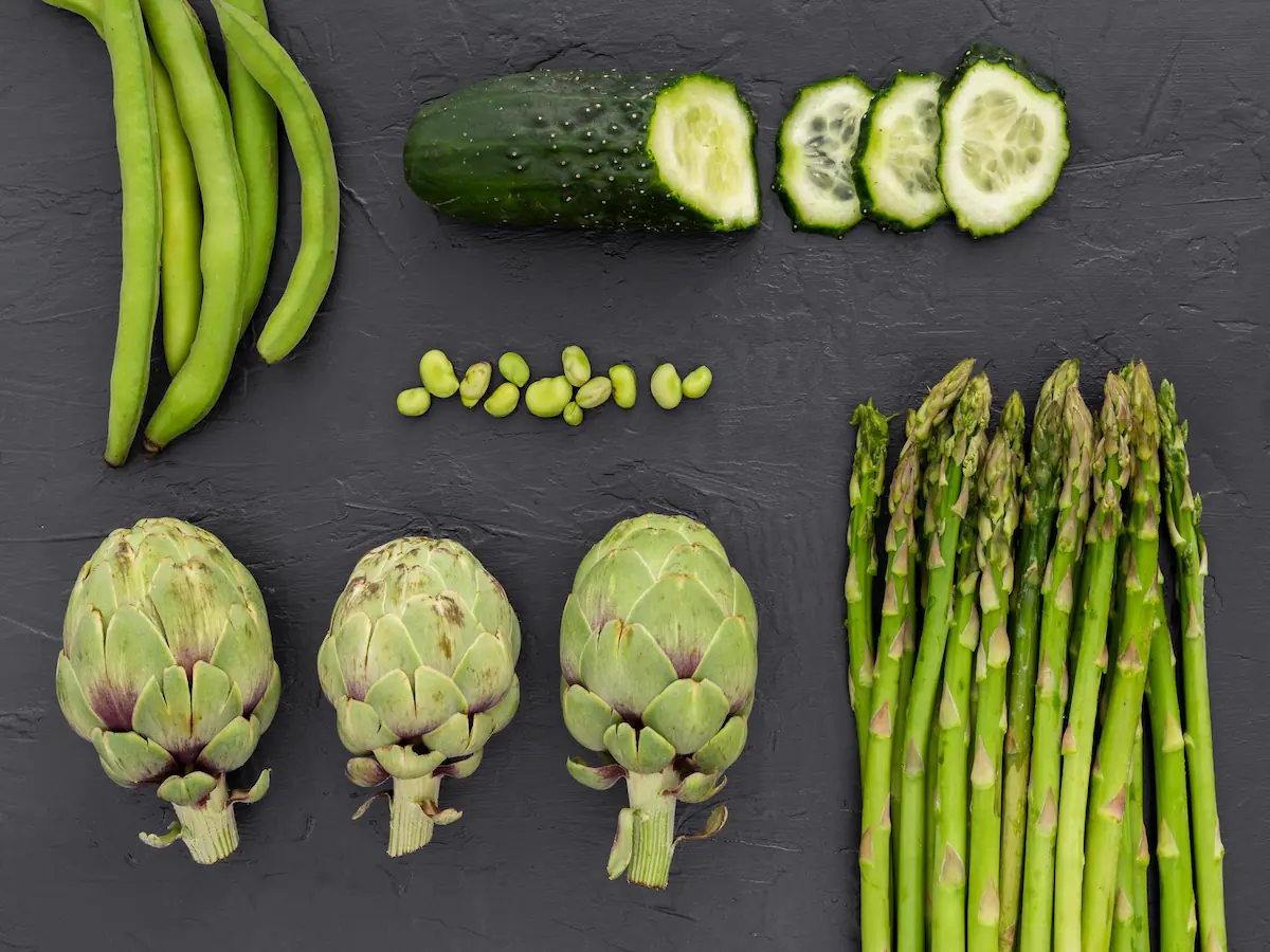 Aliments de printemps pour une détox douce : artichauts, asperges, fèves et concombre sur fond sombre