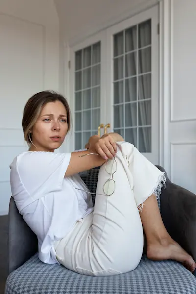 Femme assise en fauteuil, regard préoccupé, posture d'épuisement à domicile, illustrant la fatigue chronique invisible