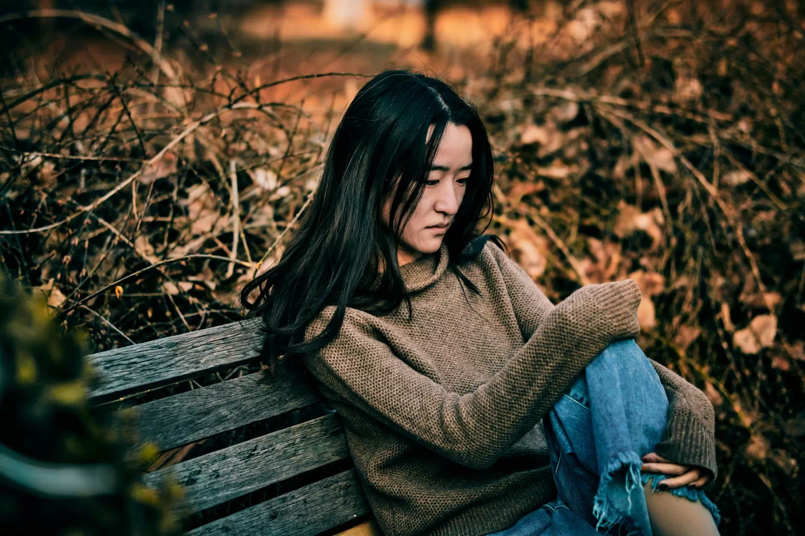 Femme pensive assise sur un banc en extérieur à l'automne, illustrant les symptômes de la fatigue et de la dépression saisonnière.