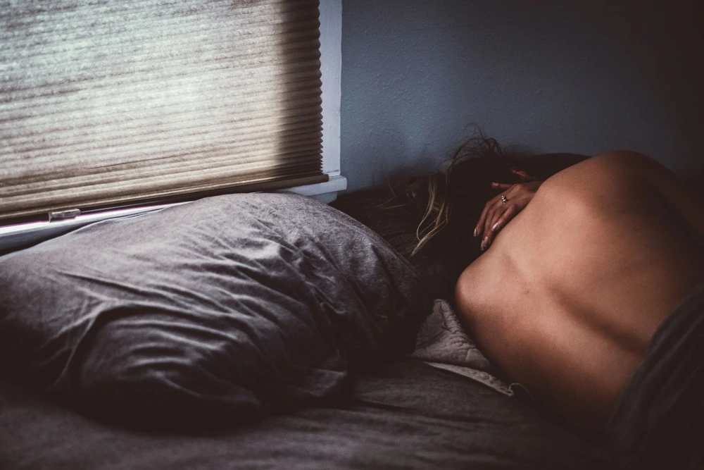 Femme allongée de dos dans un lit qui pleure. Elle incarne la perte de libido et toute la tristesse qui en découle.