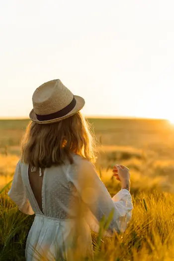 Femme de dos en robe blanche et chapeau de paille dans un champ doré au coucher de soleil, illustrant la sérénité en naturopathie