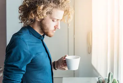 Homme pensif tenant une tasse, regard intérieur, lumière naturelle — illustrant la recherche d'équilibre au quotidien