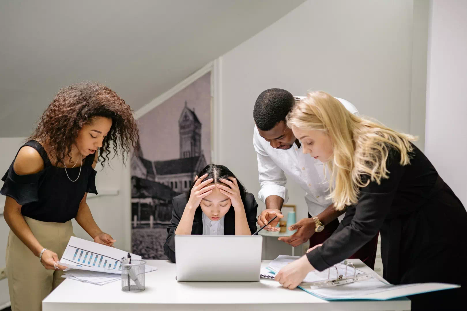 Femme au bureau exprimant des symptômes de stress chronique et de surmenage professionnel entourée de collègues.