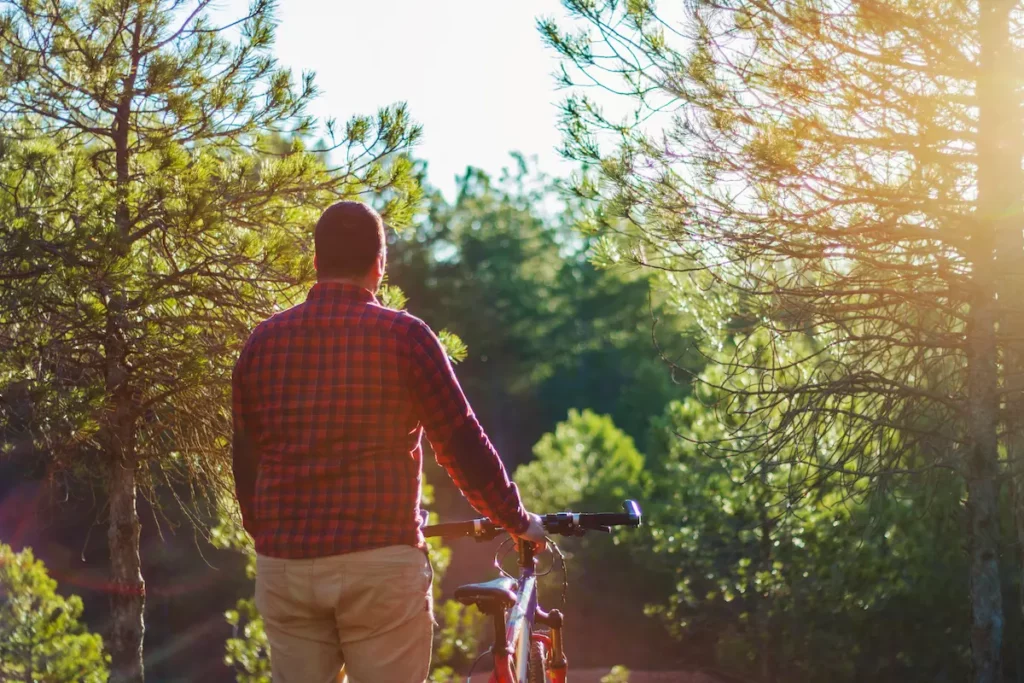 Homme de dos avec son vélo dans une forêt baignée de lumière, illustrant la reprise d'une activité physique adaptée après 45 ans